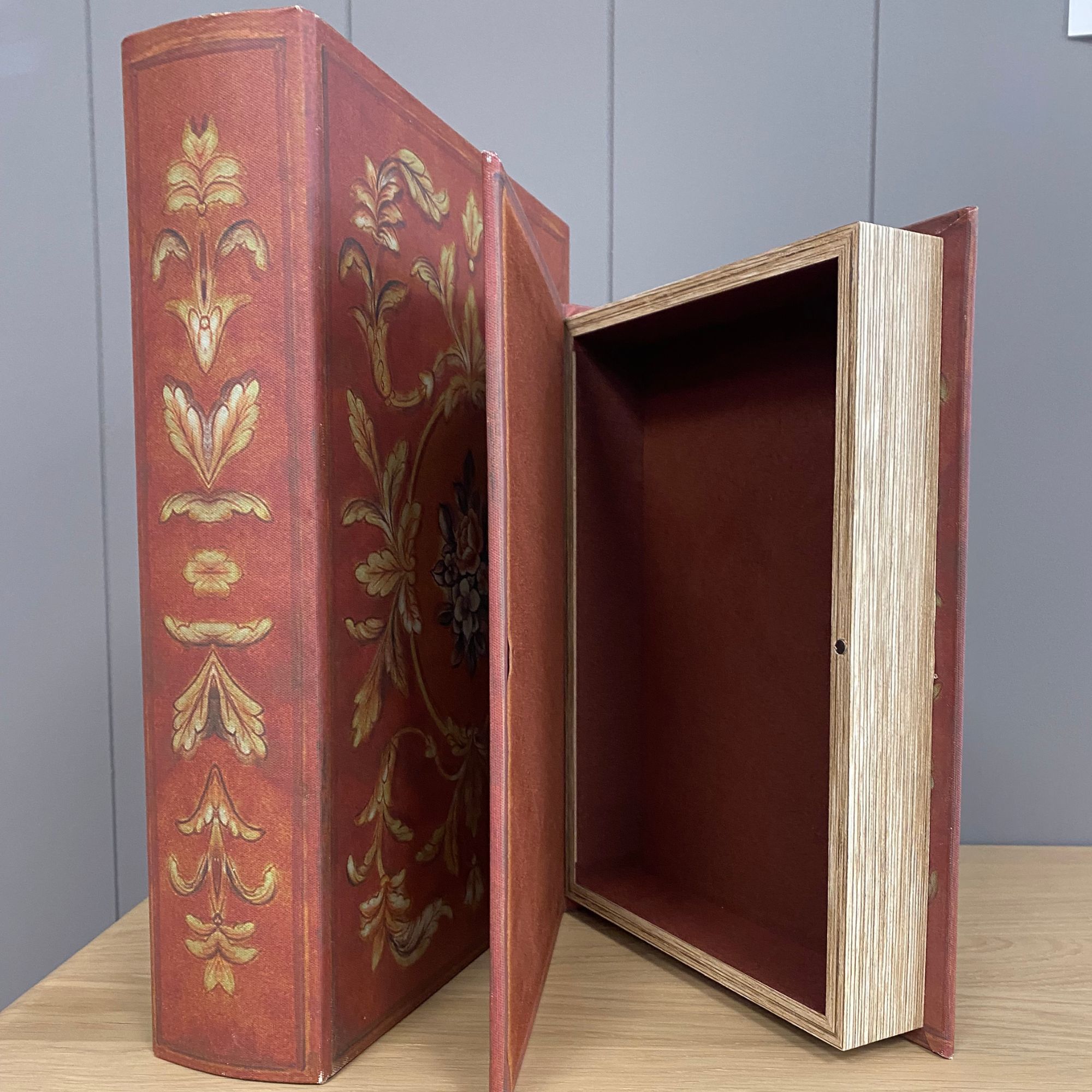 Two red and gold decorative faux book storage boxes on a wooden table. Edmunds Clarke Furniture