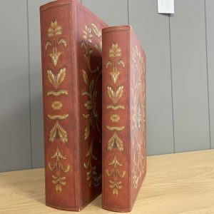 Two red and gold decorative faux book storage boxes on a wooden table.